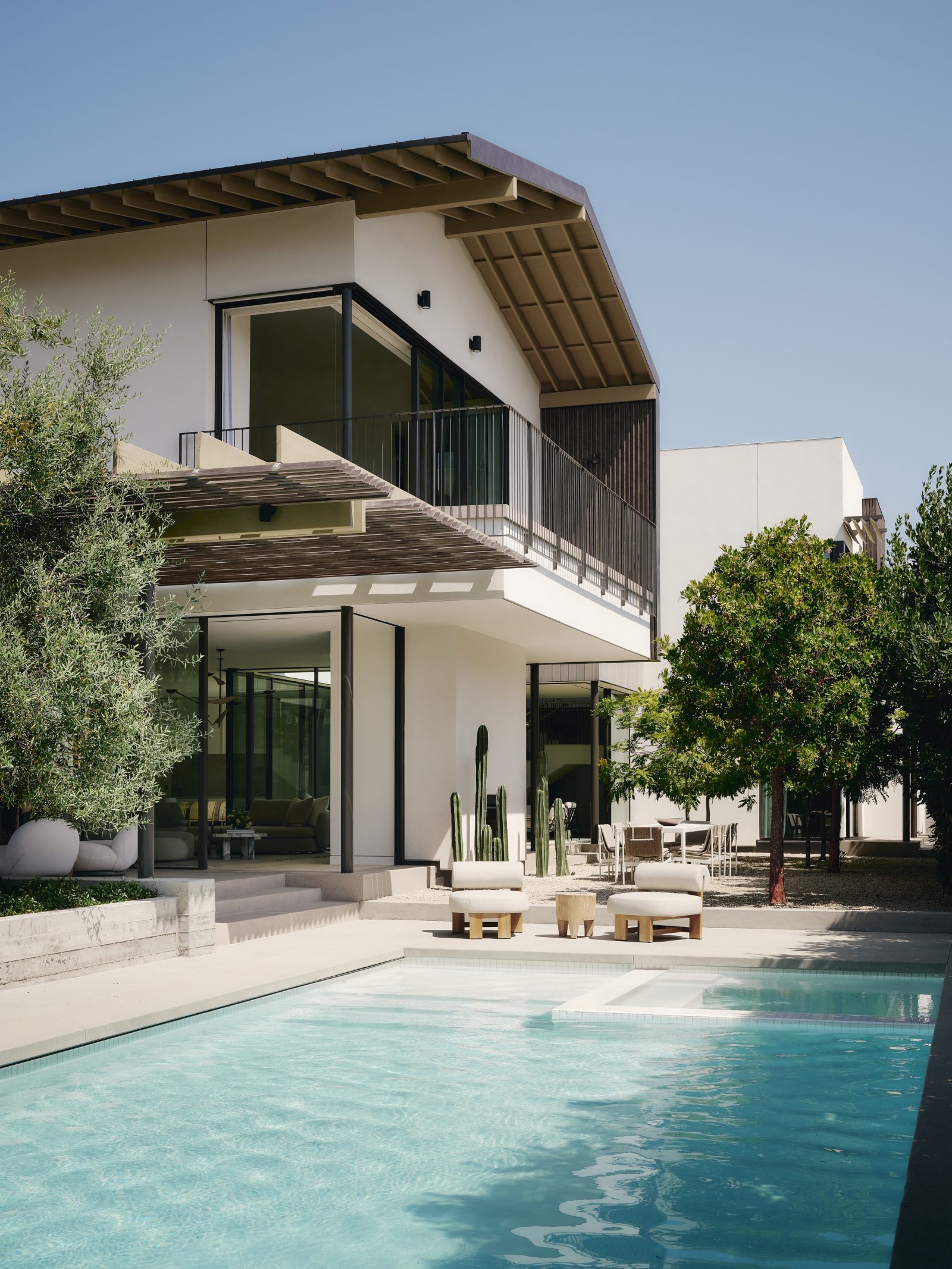 Moreno Residence pool courtyard in Brentwood with expansive glazing, deep roof overhangs, second-story balcony, and landscaped outdoor living spaces.