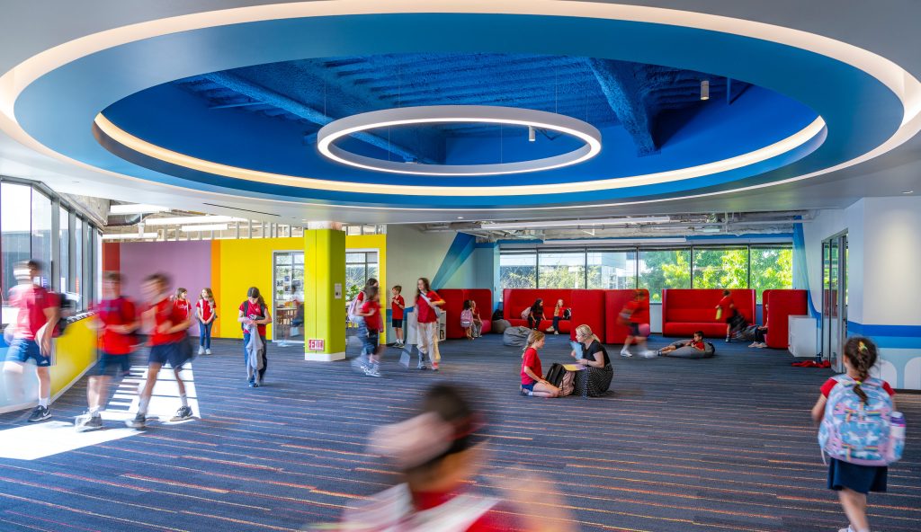 Children walking and playing beneath a circular blue ceiling feature at Village School in Santa Monica.